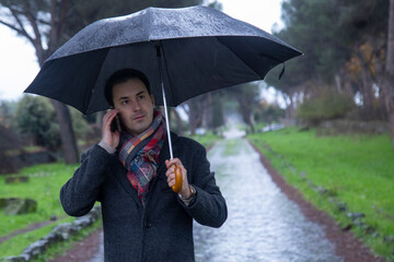 young  elegant man with umbrella talking on the phone in the rain
