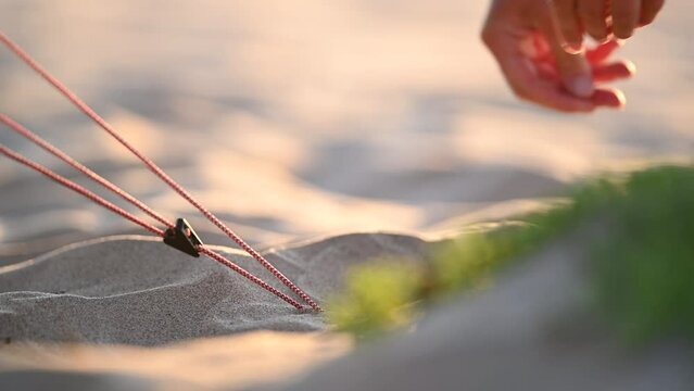 Person pushing a stake into the sand in the beach for camping and setting up a tent after a nature activity or a hike.