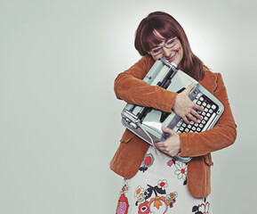My precious.... Studio shot of a bookish young woman in retro clothing hugging her typewriter.