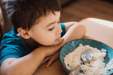 Boy sitting at table don't want to eat meal in kindergarten. Boy don't want breakfast. Healthy food.