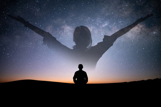 Silhouette of young female sitting practices yoga and meditating in lotus position alone on top of the mountain with night sky, star, Milky Way. She felt calm and happy..
