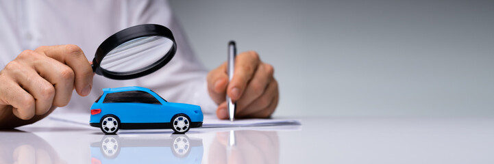 Person Scrutinizing A Car Model Using Magnifying Glass