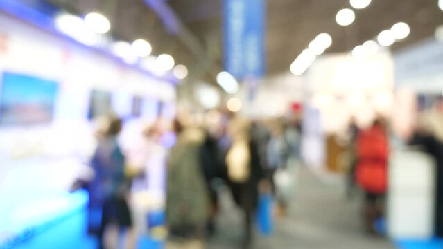 Trade show or expo fair full of people in the convention center. Out of focus blurry room with crowd of business people or shopping mall visitors. Busy exhibition hall, lots of people walking around