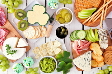 St Patricks Day theme charcuterie table scene against a white wood background. Assorted cheese, meat, fruit and vegetable appetizers. Overhead view.