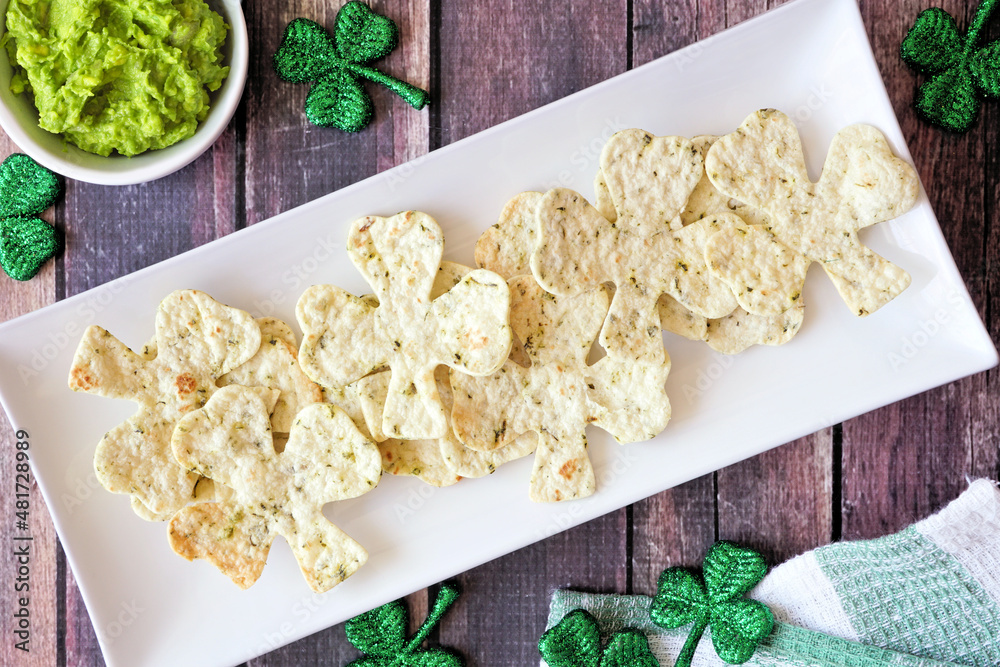 Poster st patricks day shamrock nacho chips with guacamole. overhead view on a plate against a rustic dark 