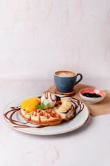 waffles with strawberries peach, kiwi, ice cream and coffee on table
