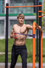 Obraz premium Young shirtless man having resistance band workout outdoor