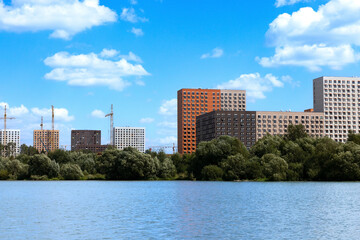Fototapeta premium New modern residential apartment buildings under construction near the lake surrounded by green trees and grass
