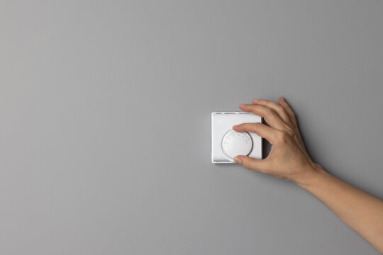 Woman Hand Adjusting or Turning On  Off Wall Temperature Regulator Controller Button on gray background