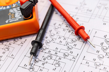 Orange digital electronic multimeter with black and red measurement probe connectors on the paper sheet with principal electric diagram. Shallow focus.