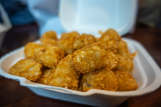 Selective Focus Of Crispy, Golden Brown Tater Tots In A White Styrofoam To-go Container From A Restaurant.