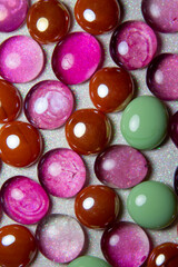 Macro abstract texture background of bright pink and light green color dragon tear glass beads on a white glittery surface