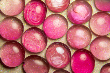 Macro abstract texture background of bright pink and light green color dragon tear glass beads on a white glittery surface