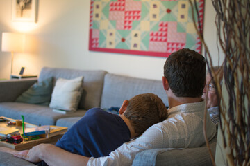 Uncle and nephew snuggle up on the couch; in the background is a family room with colorful abstract art on the wall