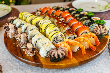 Assortment of rolls and sushi on a wooden board on a festive table. Rolls with salmon, shrimps, omelette, octopus, crab, unagi.