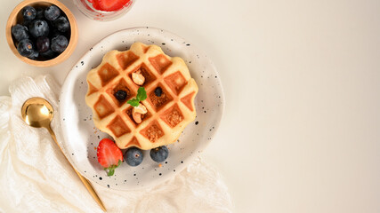Waffle with fresh berries and maple syrup on white table.