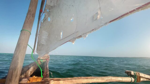 Old traditional maritime traditional vessel Dhow boat sailing under torned sail in the open Indian ocean near Zanzibar island in beautiful sunset time, Tanzania. Traveling 4K footage concept.