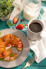 Continental breakfast. Croissant with fresh strawberries, a cup of black coffee and milk....