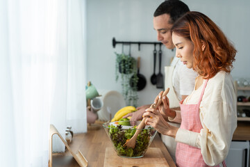 Asian beautiful woman cook green salad with husband in kitchen at home. 