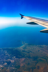 Fototapeta premium View from the airplane window at a beautiful blue clear sky, earth, sea and the airplane wing