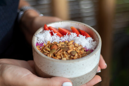 Woman holding a bowl of strawberry smoothie bowl with coconut flakes, nuts, muesli. superfood healthy concept