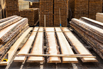The board is uncut, ready for sorting on an industrial site. Lumber production in the background.