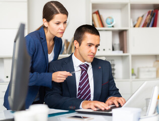 Focused male and female business colleagues looking at computer screen, discussing new project in office