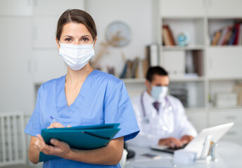 Portrait of nurse in protective medical mask with folder of documents at clinic office. High...