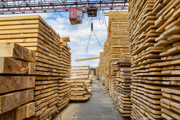 View of the lumber warehouse between stacks of boards. The background is a crane for loading wood,...