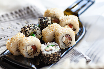 Japanese sushi food. Maki and rolls with tuna, salmon, shrimp, crab and avocado. Served on a dark glass dish from a melted black bottle