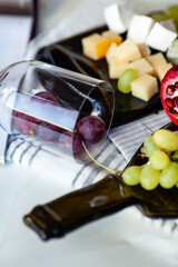 Cheese platter with different cheese and grapes, served on a glass transparent dish from a melted bottle