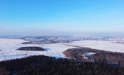 Top view of a winter landscape with a snowy field and a forest