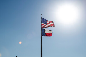 American US Flag and Texas Flag Below Waving in Wind with Bright Sun