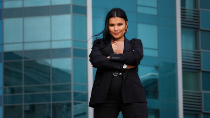 Young hispanic businesswoman employee company standing confidently arms crossed outdoors on background office building looking at camera posing in successful pose feels satisfied with career growth