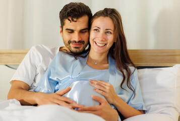 Cheerful husband enjoy embracing pregnant wife and happy to tenderly fondle beloved belly of unborn baby and expecting warm family during prenatal care of maternity at romantic bedroom