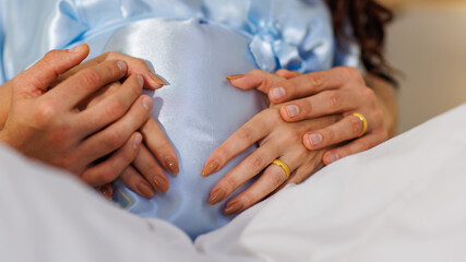 Hands of father and pregnant mother tenderly embrace and hold belly of unborn baby in shape of...