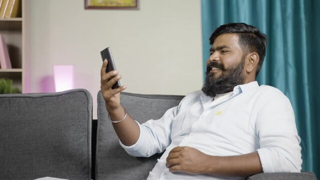 Young man busy making video call on mobile phone at home - concept otf online dating application, social media, video chat and technology