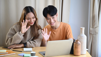 Happy young couple having video call with family on computer laptop at home.