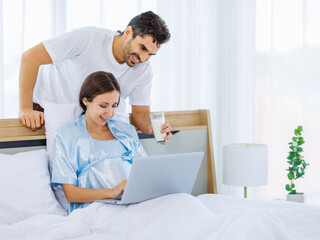 Obraz premium Lovely pregnant wife tenderly touch beloved belly of unborn baby while lounging on bed with smile and happy as enjoy watching entertainment media on computer