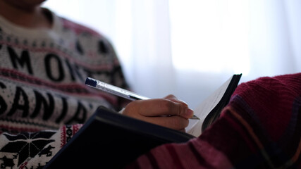 unrecognizable woman in warm knitted sweater writes down plans or tasks for the new year.