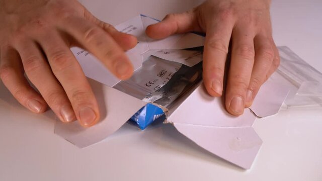 Closeup of hands opening antigen test kit and laying content on white surface table close to camera - Static closeup