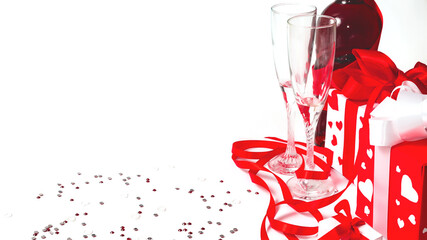 Still life with a gift box, red satin ribbon and two glasses of wine on a white background. Valentine's Day card with copy space. Design element for romantic greeting card, wedding invitation