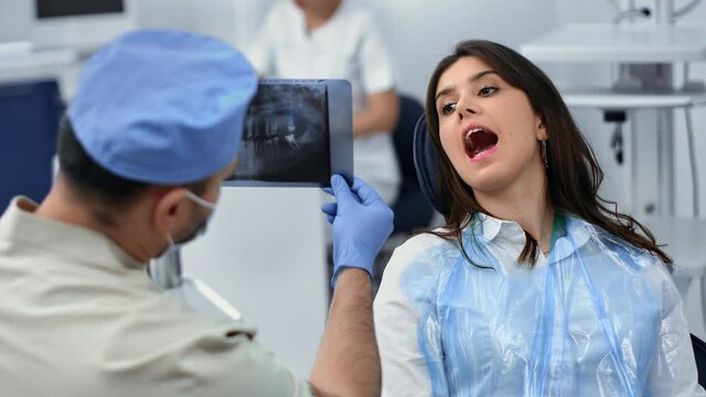 Male stomatologist analyzing x ray image denial cavity woman patient sitting chair with open mouth