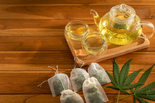 Photo of a pot of hot cannabis tea serves in wooden tray with teabag over wooden table background. Copy space for text banner artwork backdrop design. Eatable recipe health herb vegan drink concept