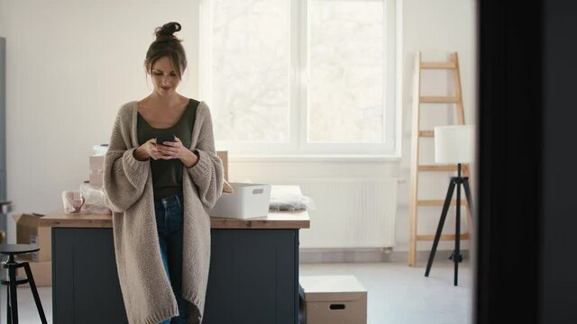 Young caucasian woman using mobile phone while unpacking stuff in new house. Shot with RED helium camera in 8K
