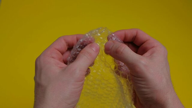 Stress concept. Man's hands popping bubbles from a bubble popper on yellow table. 