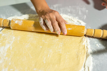 close-up. rolled dough lies on the table. a rolling pin lies on the test, it is held by a female hand. all in flour