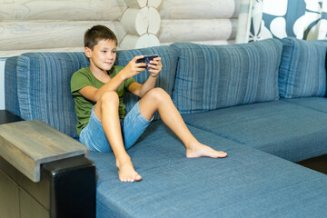 Obraz premium boy at home with a phone sitting on a sofa. kids and gadgets