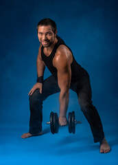 muscular man with dumbbells. sportsman posing in black t-shirt, jeans with dumbbells. studio...