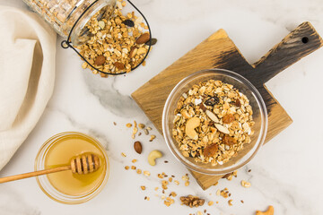 baked granola or muesli with nuts, dried fruits and honey in a glass bowl on a wooden board. top view. marble background.